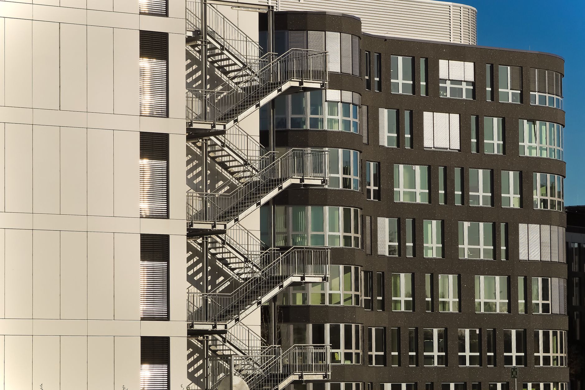 A contemporary building facade with steel staircases and glass windows under clear skies.