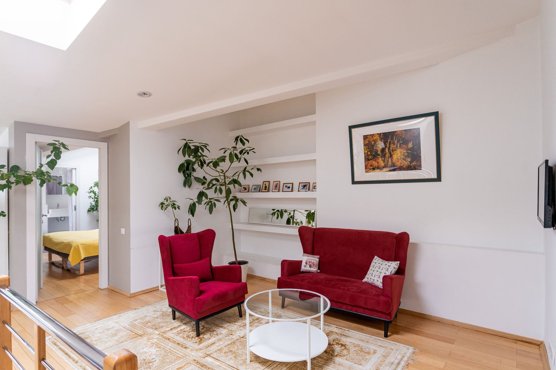 Bright living room featuring red armchairs, white walls, and lush plant decor.
