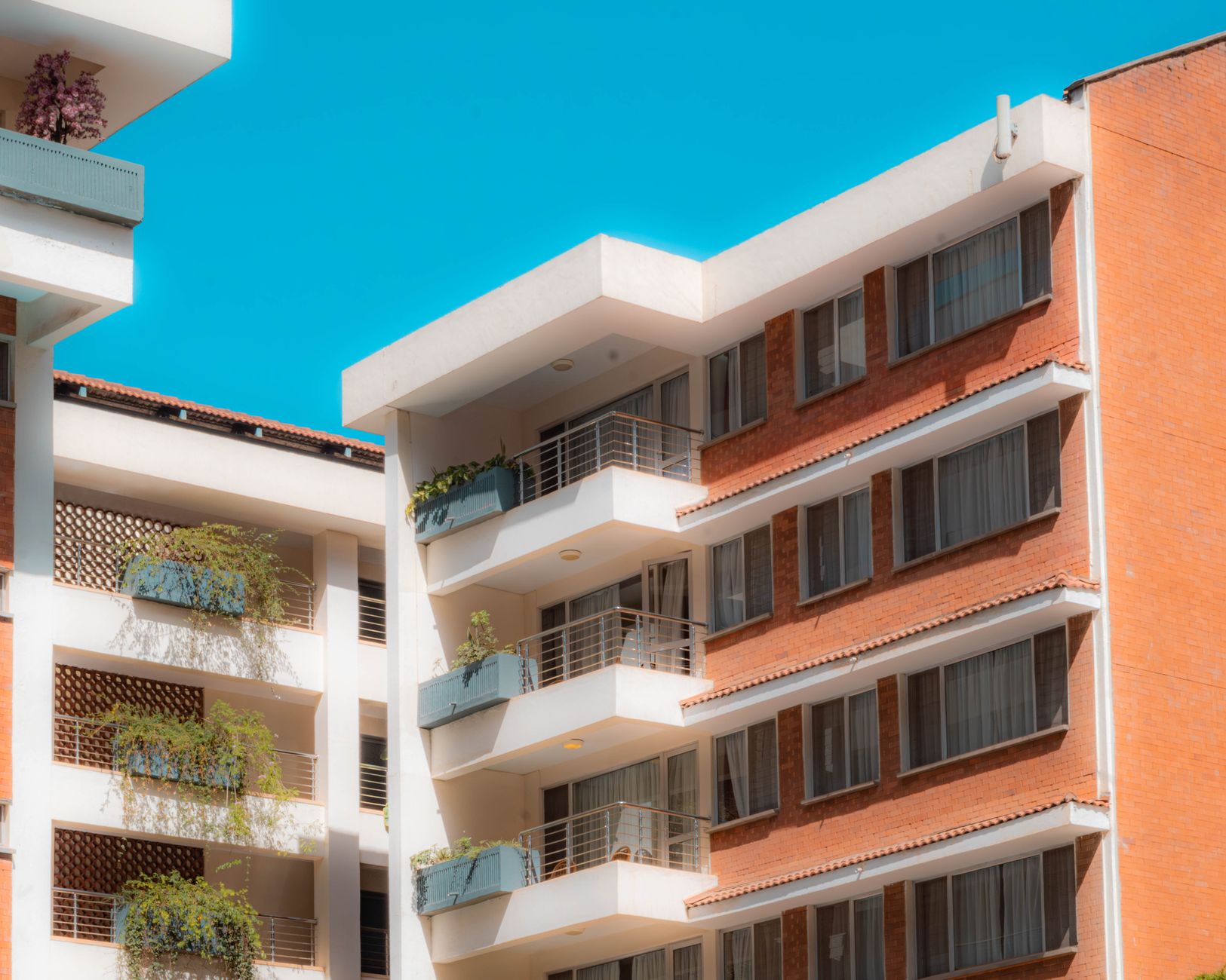 Bright and sunny view of contemporary apartment buildings with balconies and plants under a clear blue sky.