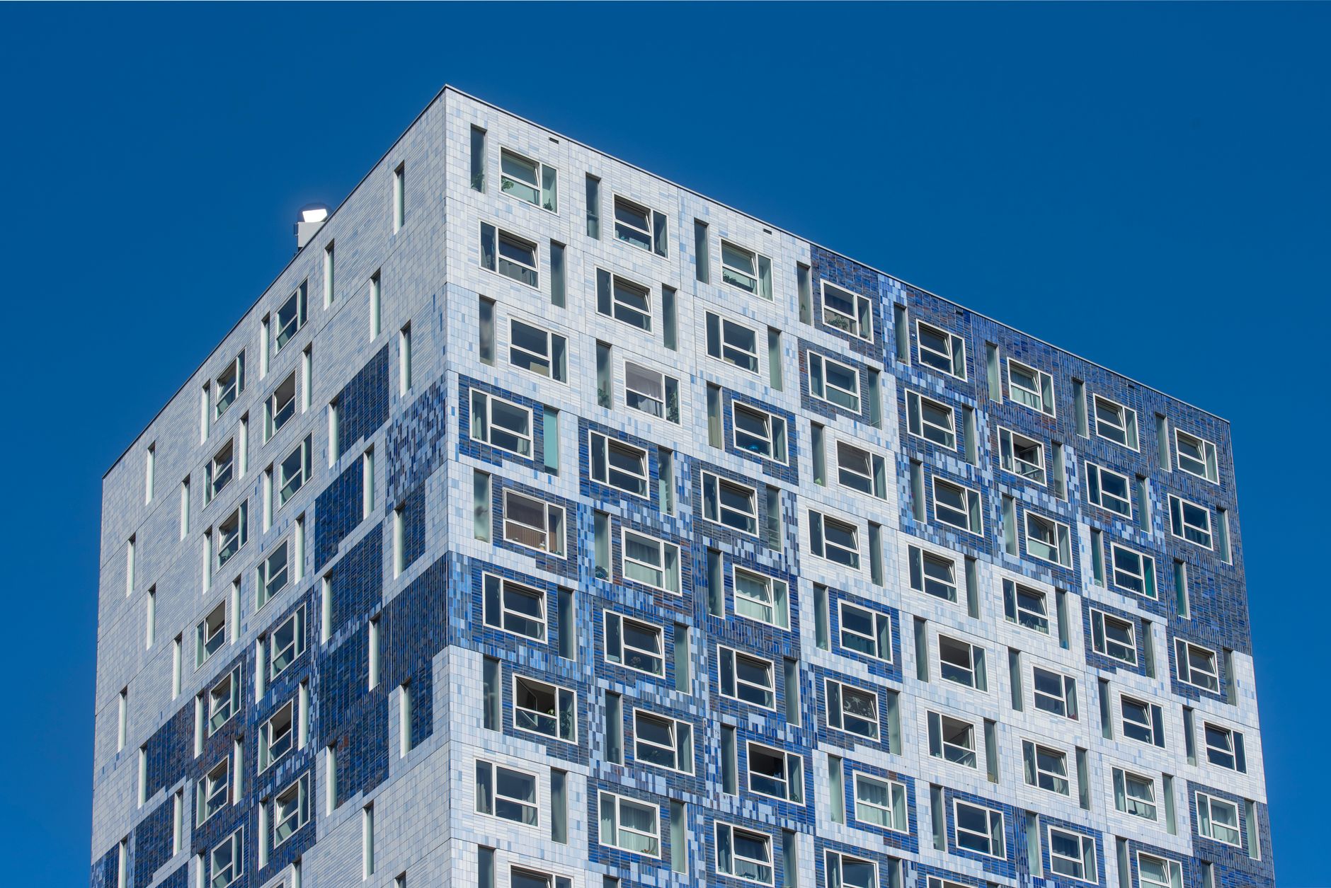 A modern high-rise building with a mosaic facade captured against a clear blue sky.