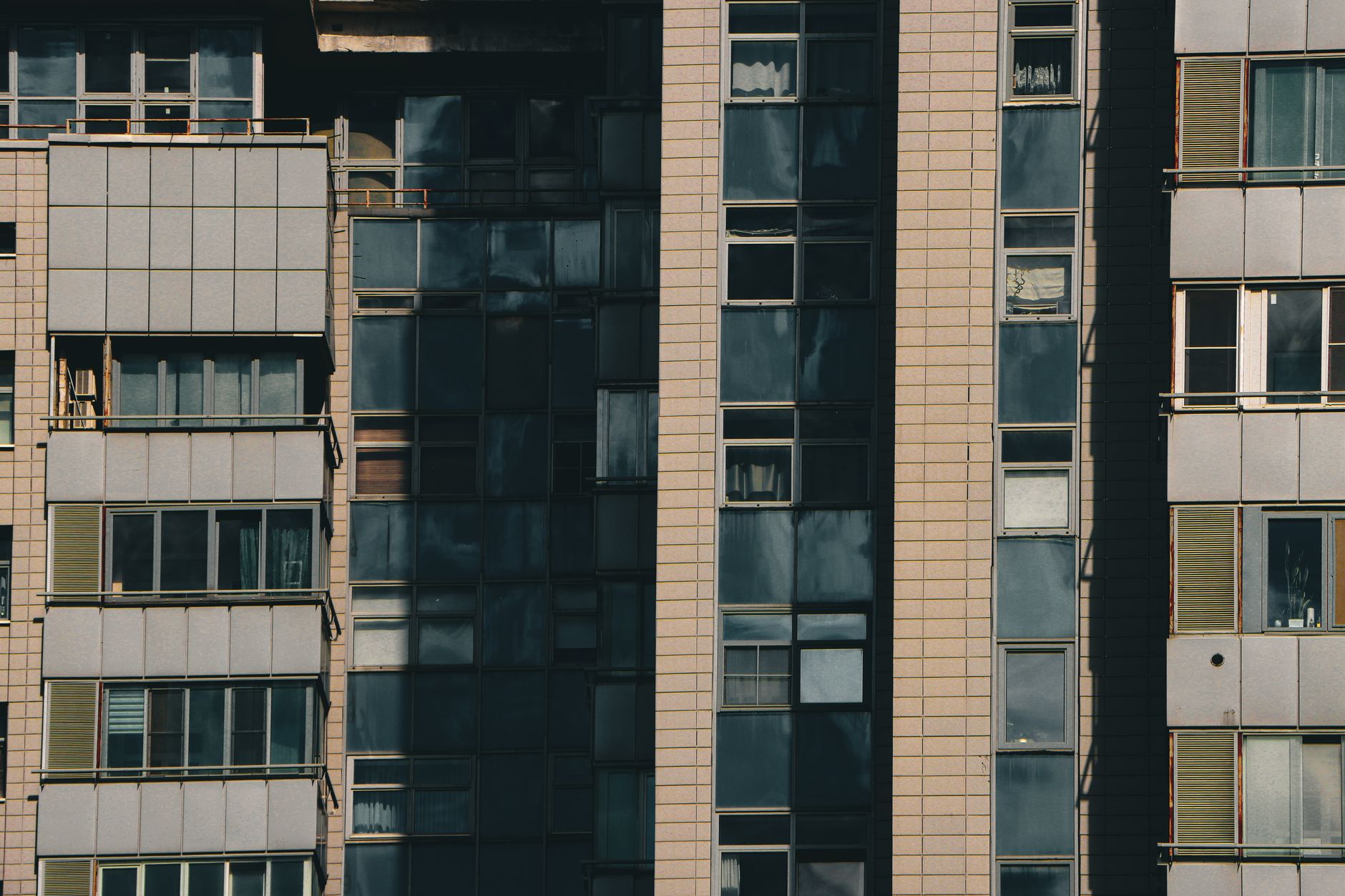 Close-up view of a modern apartment building with diverse window designs and tiled facade in an urban setting.