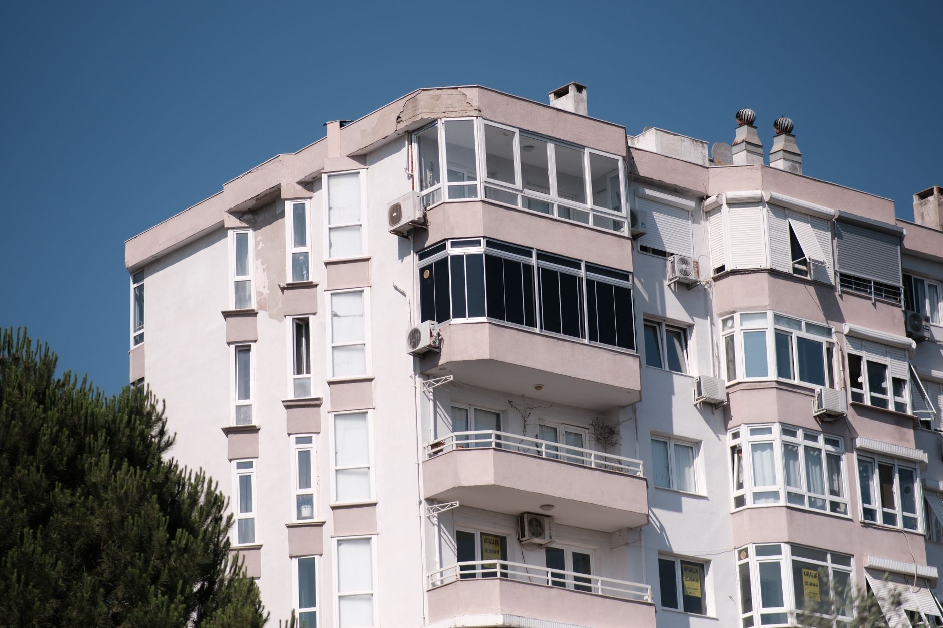 White apartment building with balconies and air conditioning units, located in İzmir, Türkiye.