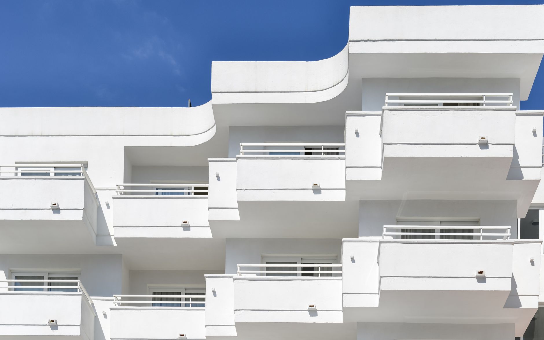 Stylish modern architecture of a white residential building with balconies against a clear blue sky.