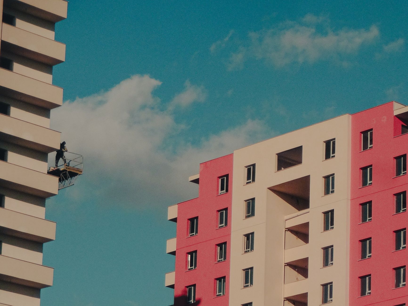 Colorful high-rise buildings with a worker on a suspended platform against a clear sky.