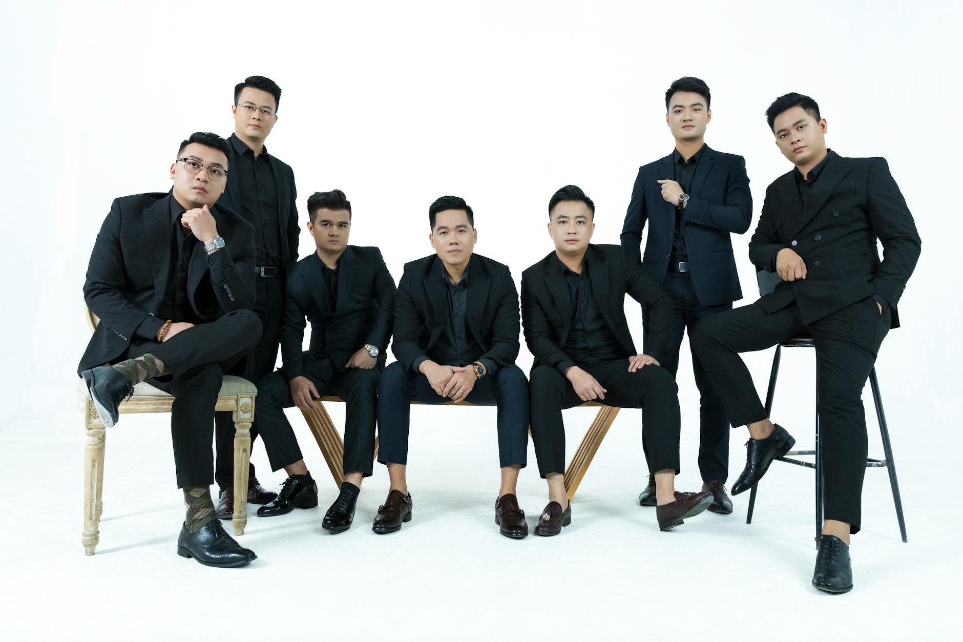 A stylish group of men in suits posing elegantly against a white backdrop in a studio setting.