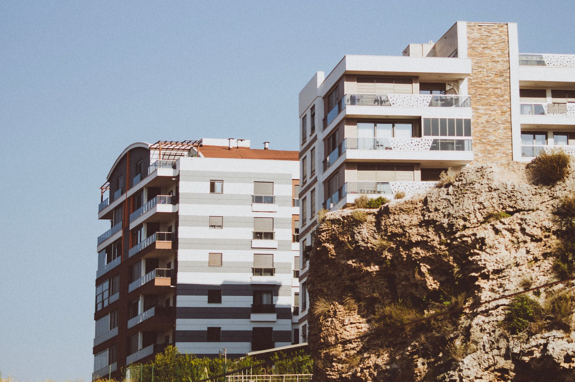 Stylish modern apartments perched near a rocky cliff under a clear blue sky.