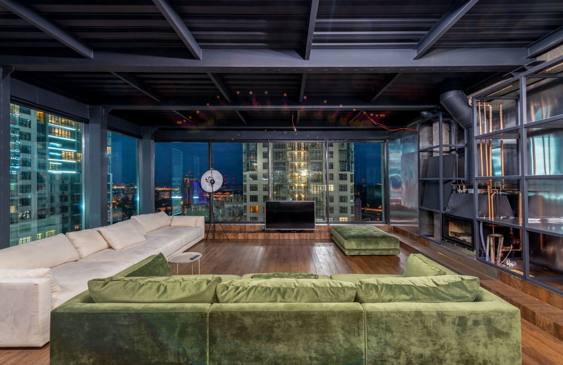 Interior of contemporary spacious living room with large comfortable sofas and panoramic windows in evening time