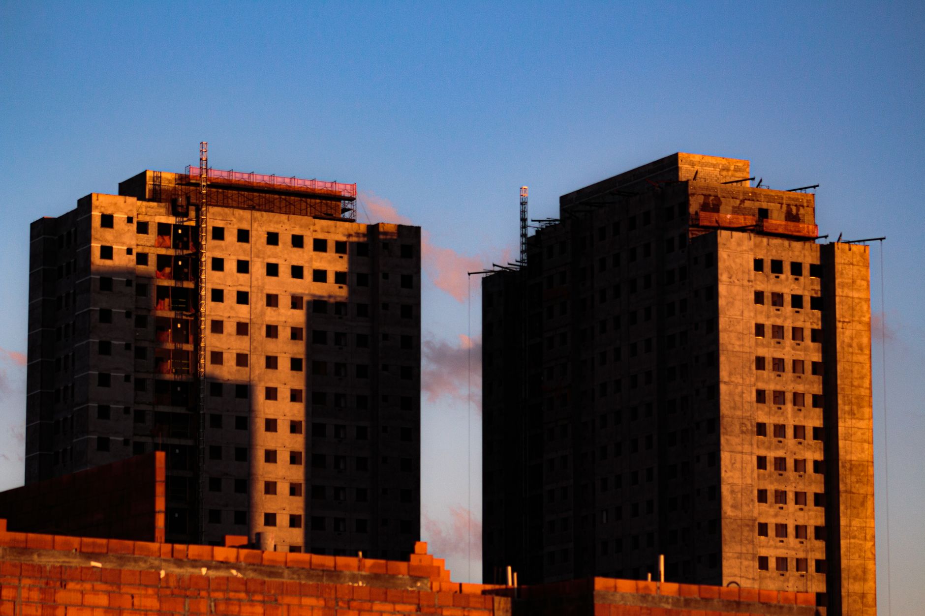 From below of tall concrete houses under construction at sunlight against blue sky