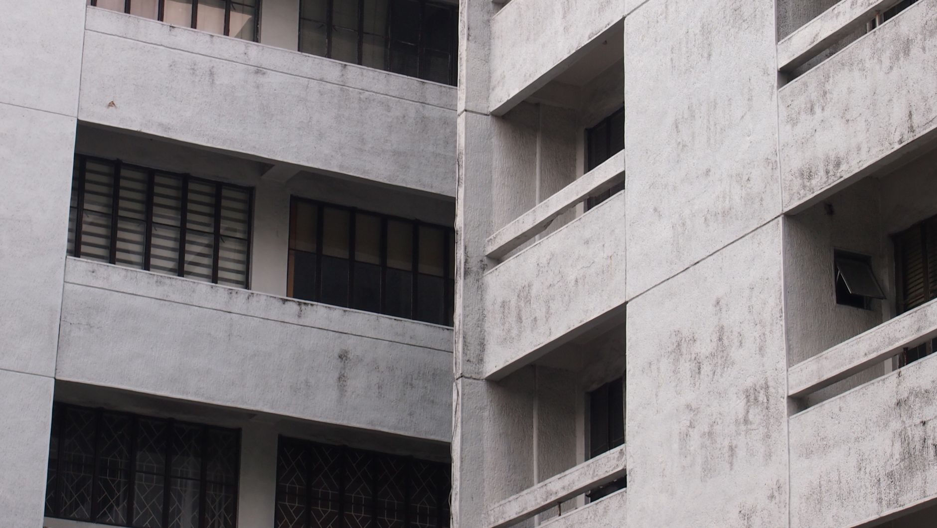 Close-up of a gray concrete apartment building facade with windows.