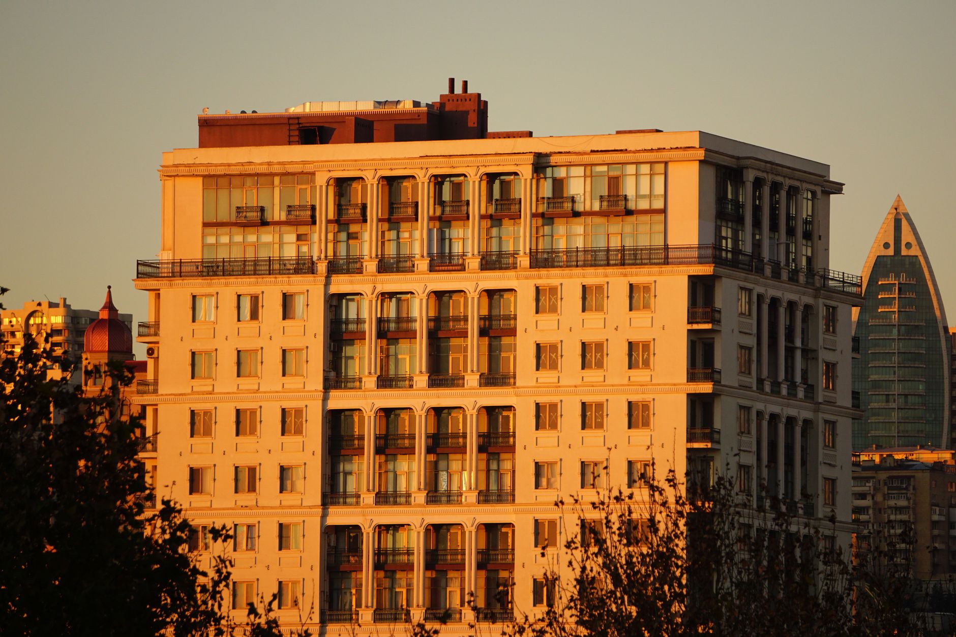 Golden hour view of an urban apartment building with sunlit façade and cityscape backdrop.