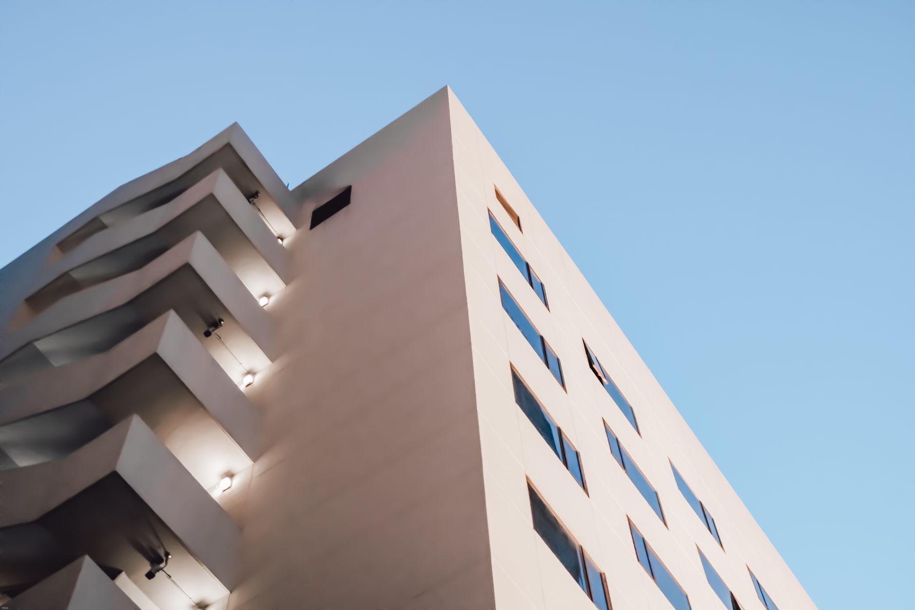 Abstract view of modern building facade with balconies and windows under clear blue sky.