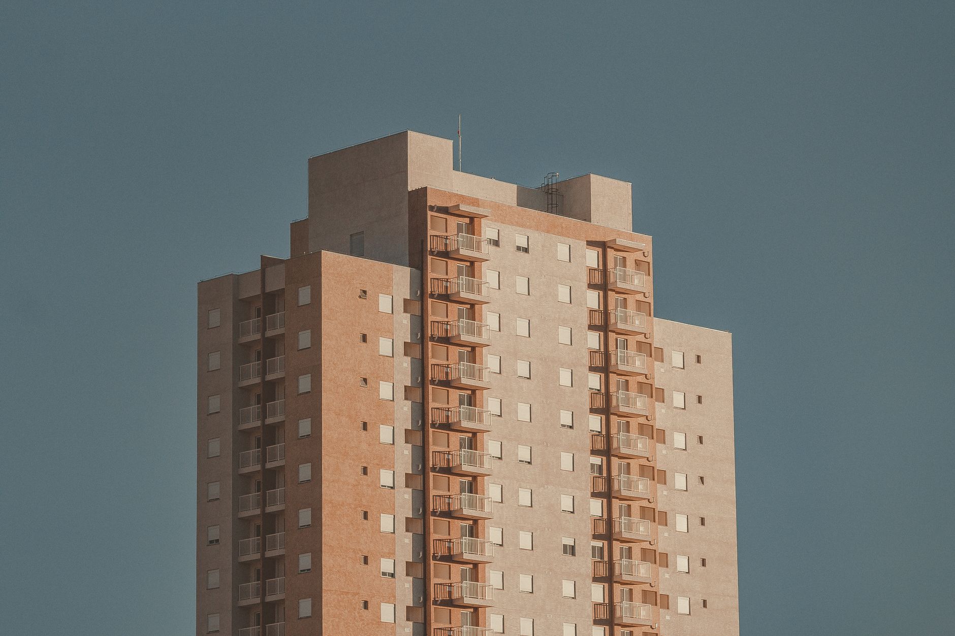 A modern high-rise building with a facade featuring uniform windows and balconies set against a clear blue sky.