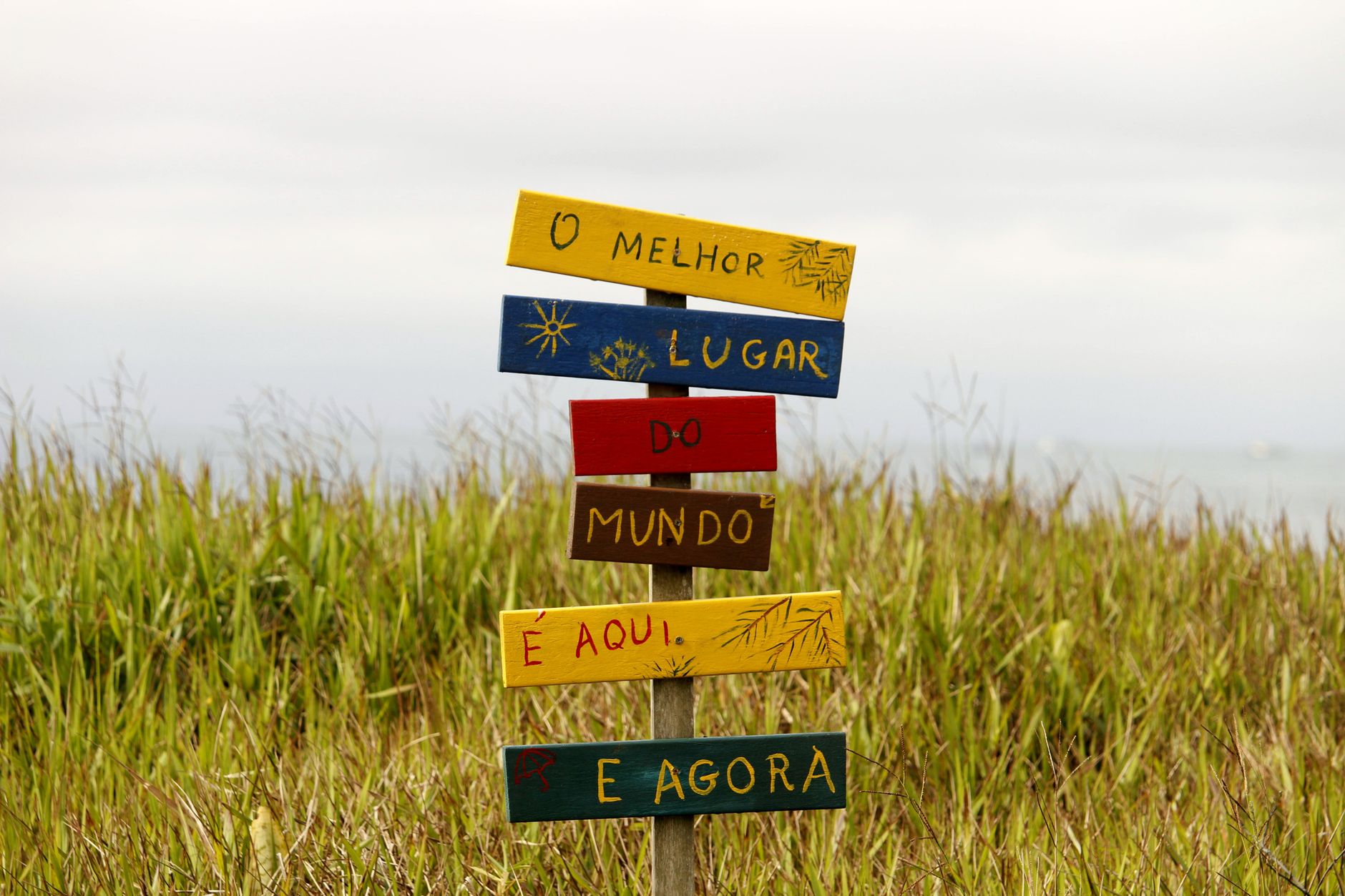 Vibrant multilingual sign in a grassy field in Guaratuba, Paraná, Brazil, showcasing local charm.