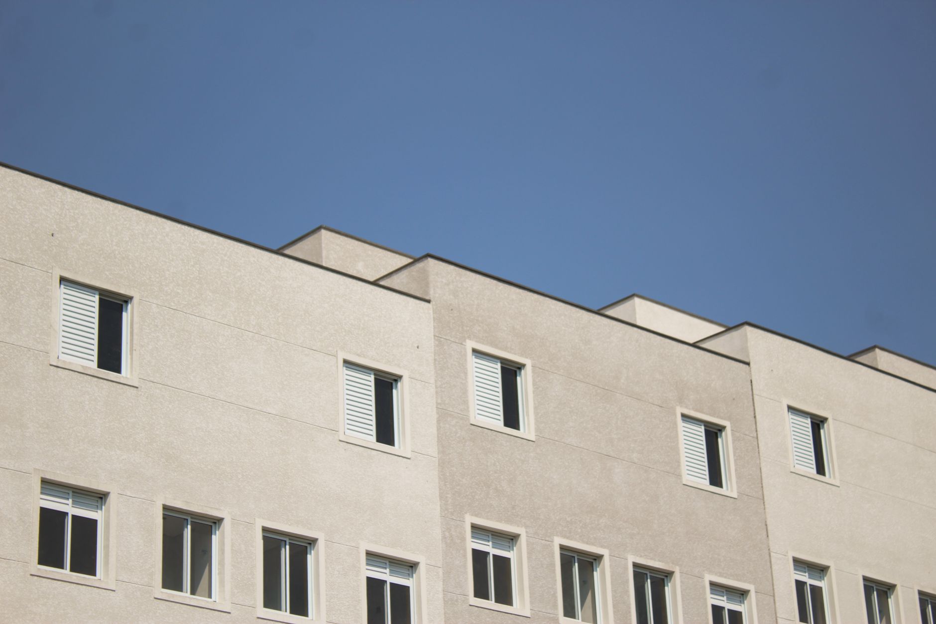 Minimalist urban building design with a focus on concrete facade and windows under a clear blue sky.