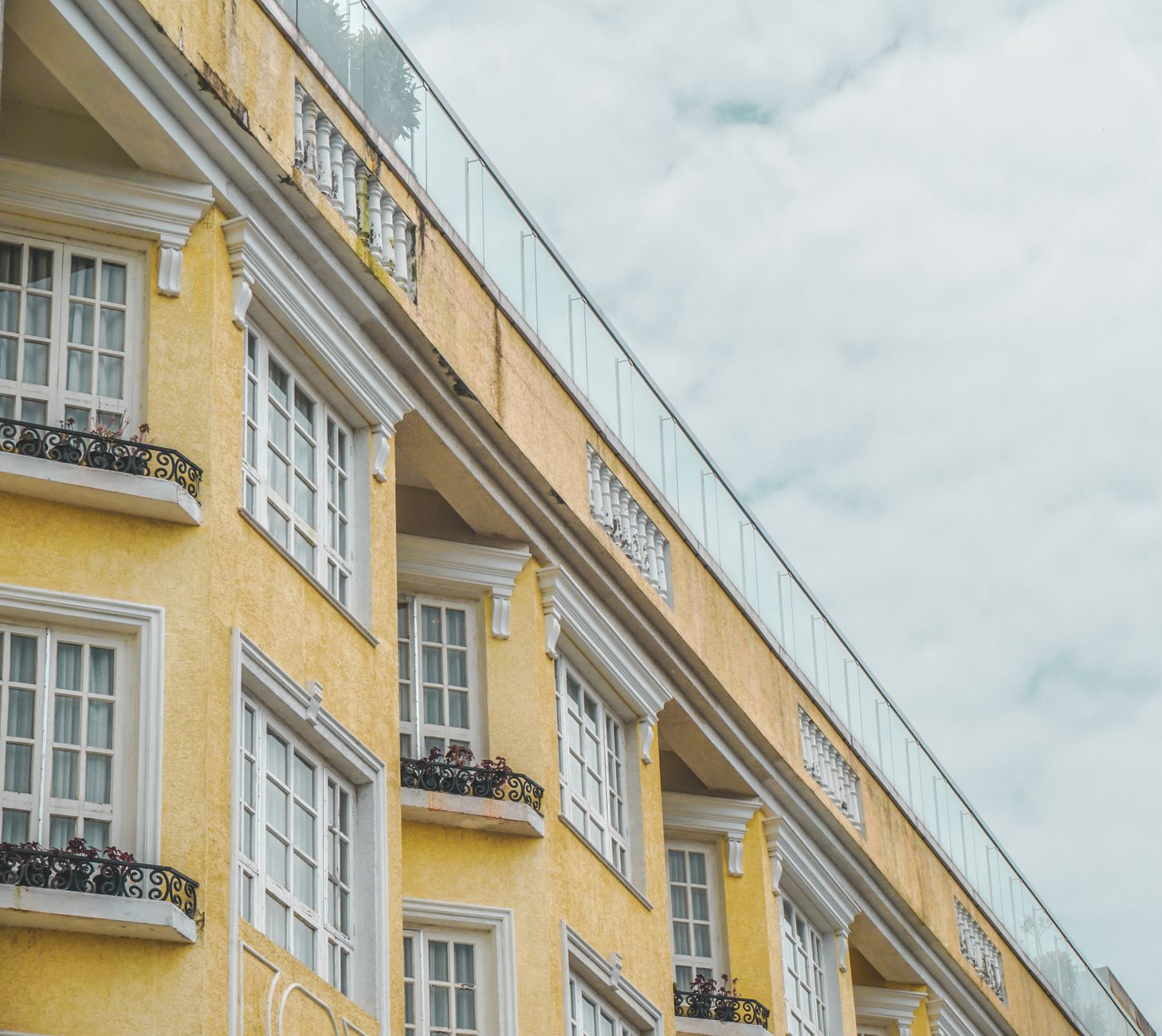 Close-up of yellow building facade with decorative elements and balconies under a cloudy sky.