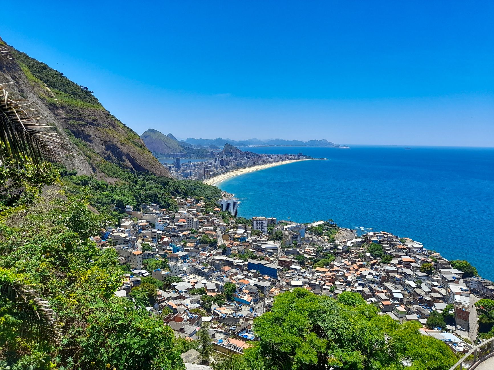 Expansive aerial view of Rio de Janeiro's coastline with clear blue skies and ocean, lush greenery, and cityscape.