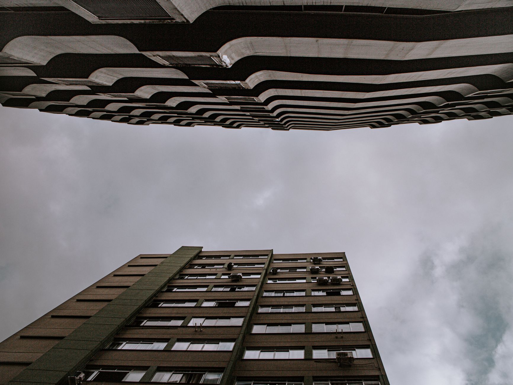 Dramatic low-angle view of urban skyscrapers under a gray, overcast sky.