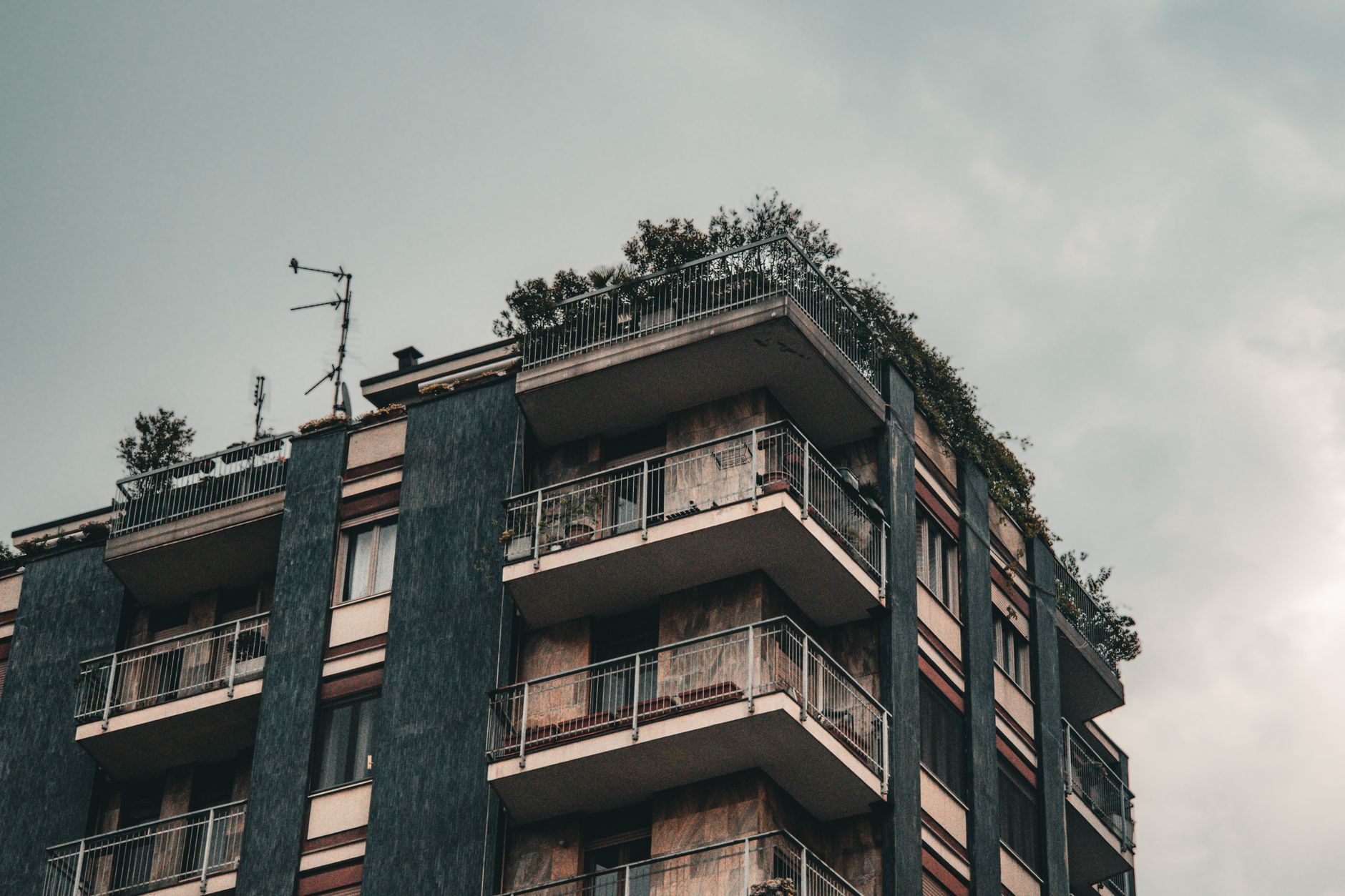 Urban building with balconies in Milan, showcasing modern architecture and a cloudy sky.