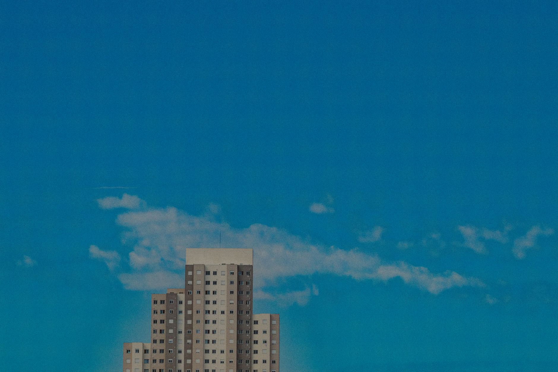 Facade of high multistory residential condominium located in living district against bright blue sky with clouds