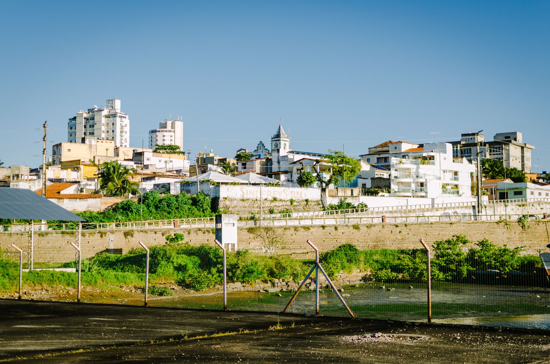 Cityscape featuring residential buildings under a clear blue sky with visible fencing.