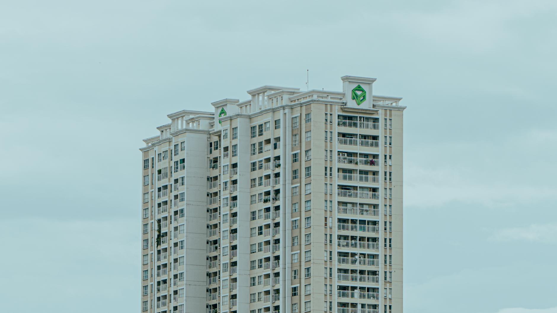 A tall modern apartment building stands against a cloudy sky, showcasing urban architecture.
