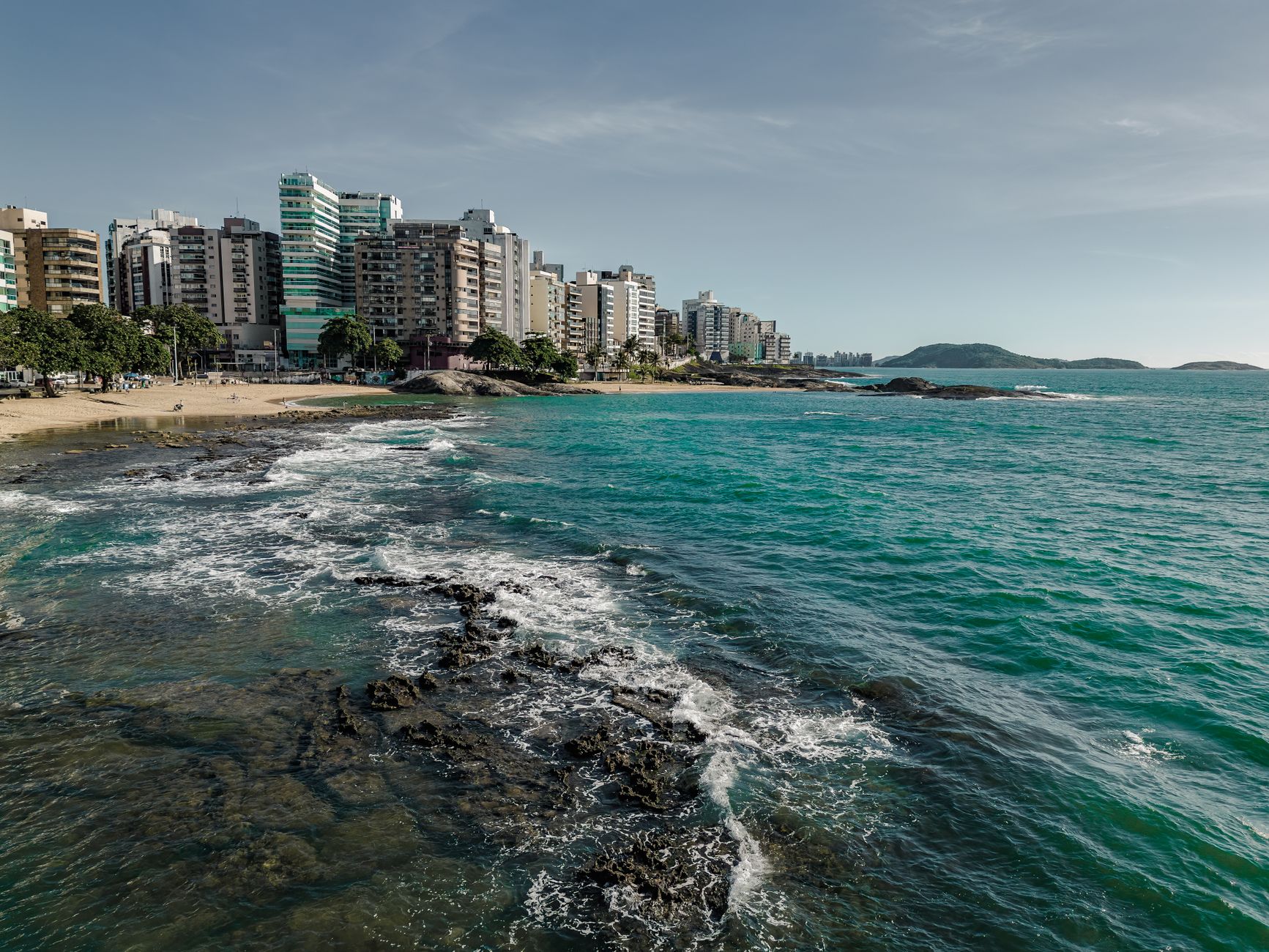Scenic view of Guarapari's coastline with urban skyline and clear blue waters in Brazil.