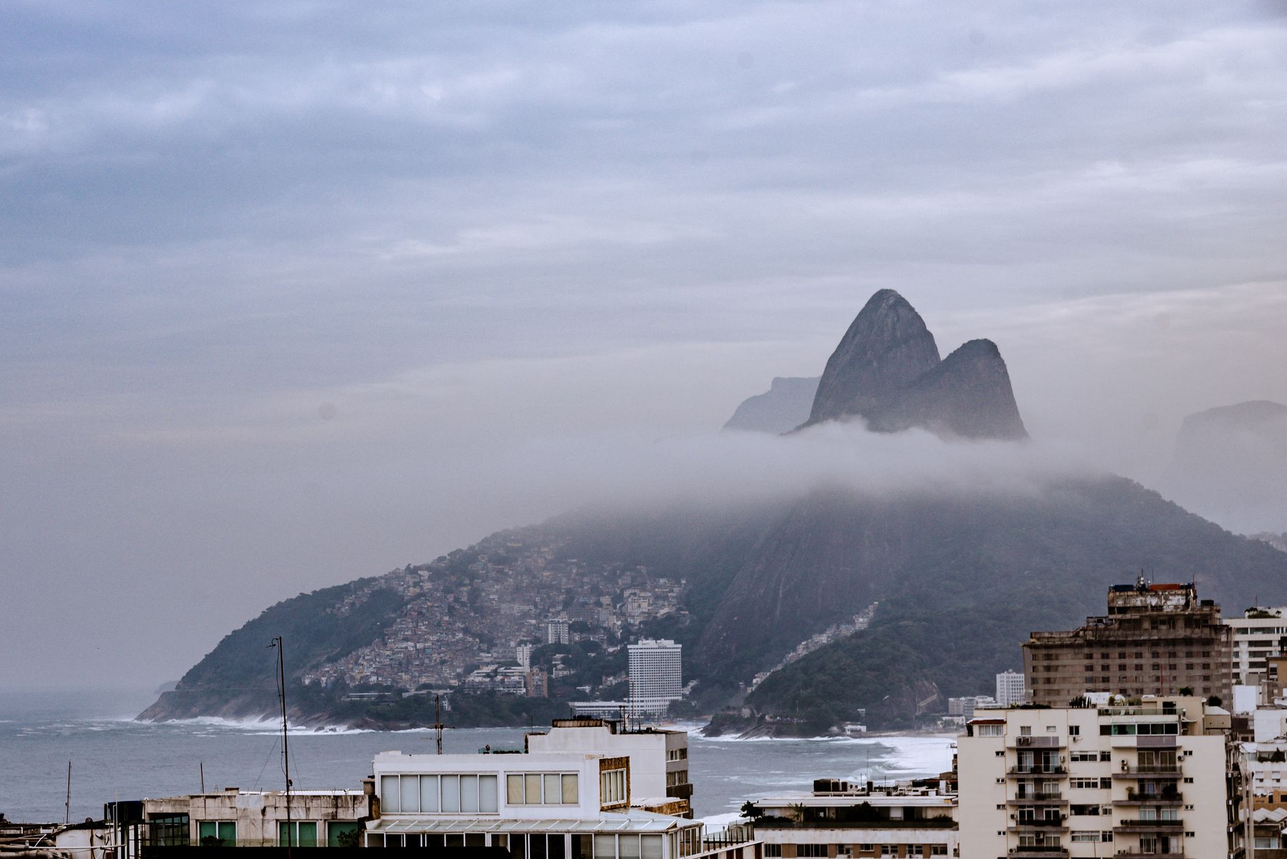 A foggy morning view of the iconic Two Brothers Hill in Rio de Janeiro, Brazil, showcasing modern architecture and coastline.