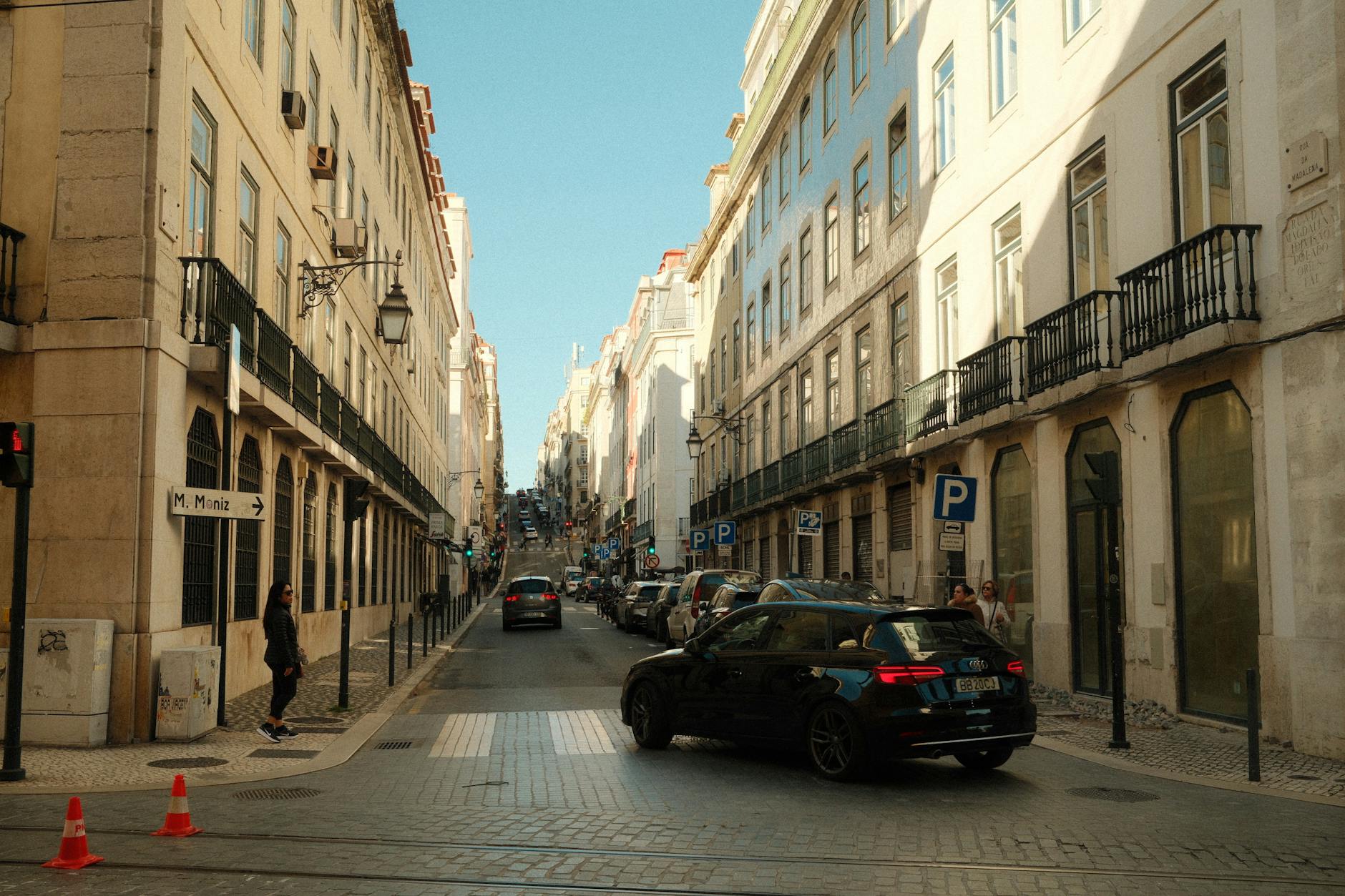 Scenic view of a bustling street in Lisbon with classic architecture and parked cars.