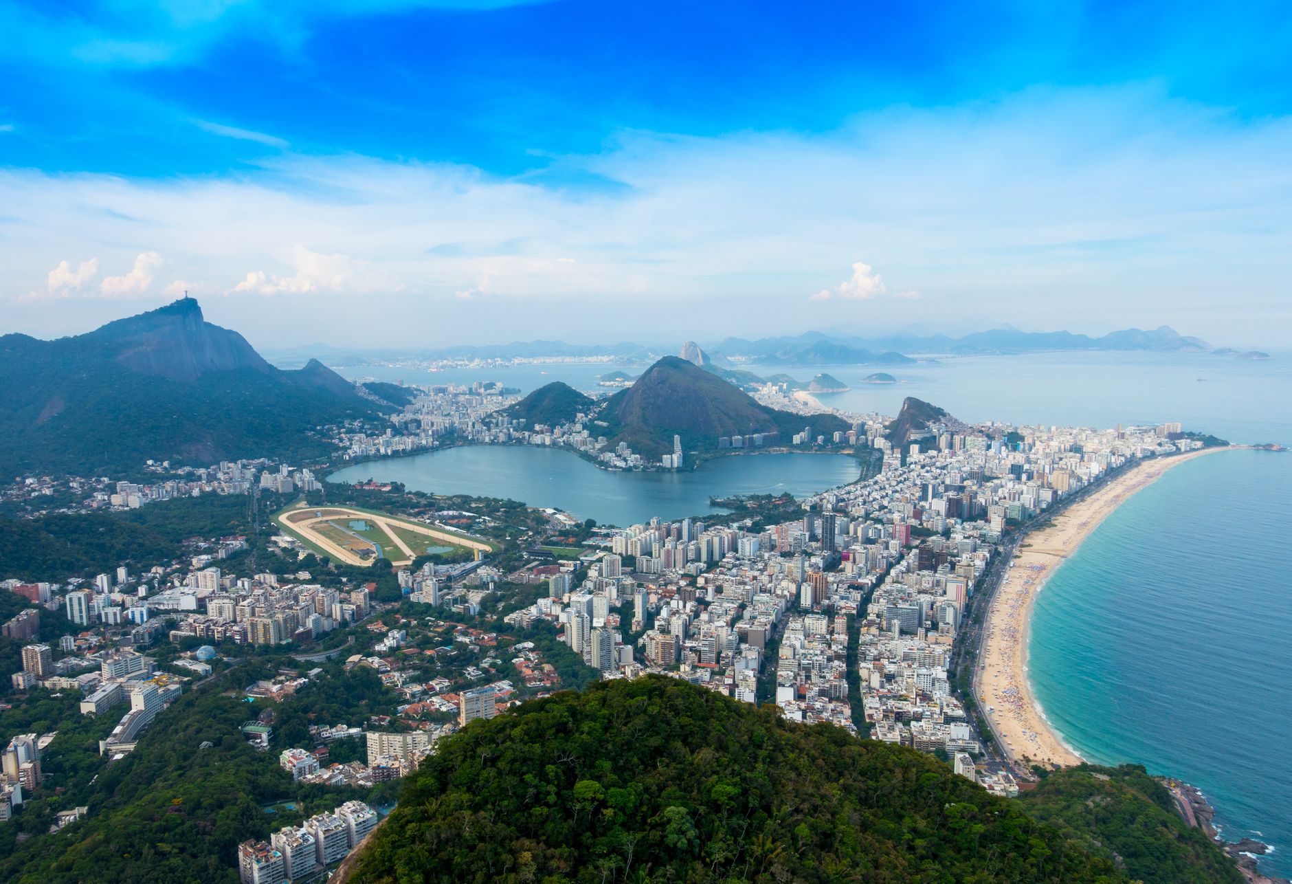 Panoramic aerial view of Rio de Janeiro's coastline, iconic landmarks, and lush mountains.
