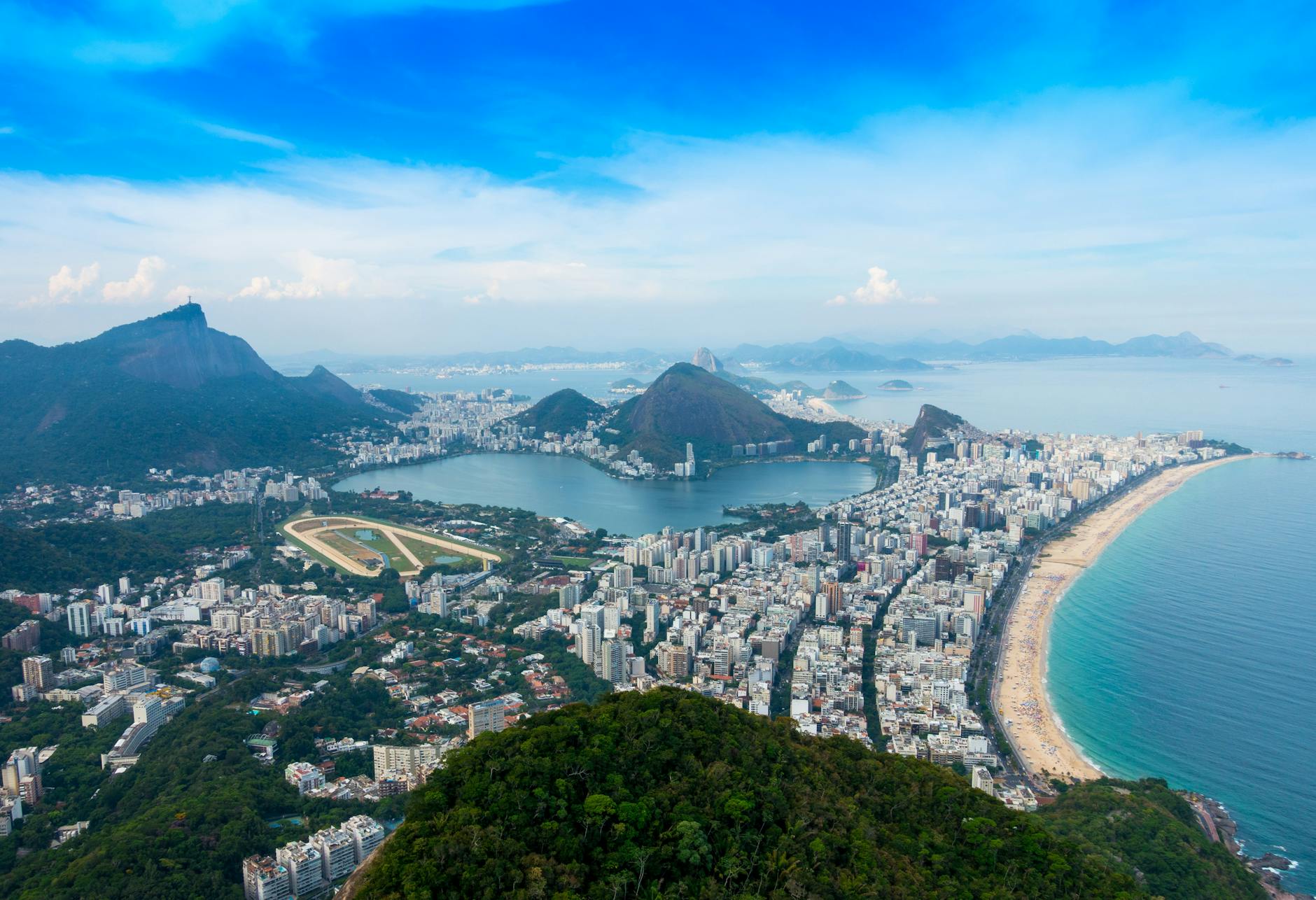 Panoramic aerial view of Rio de Janeiro's coastline, iconic landmarks, and lush mountains.