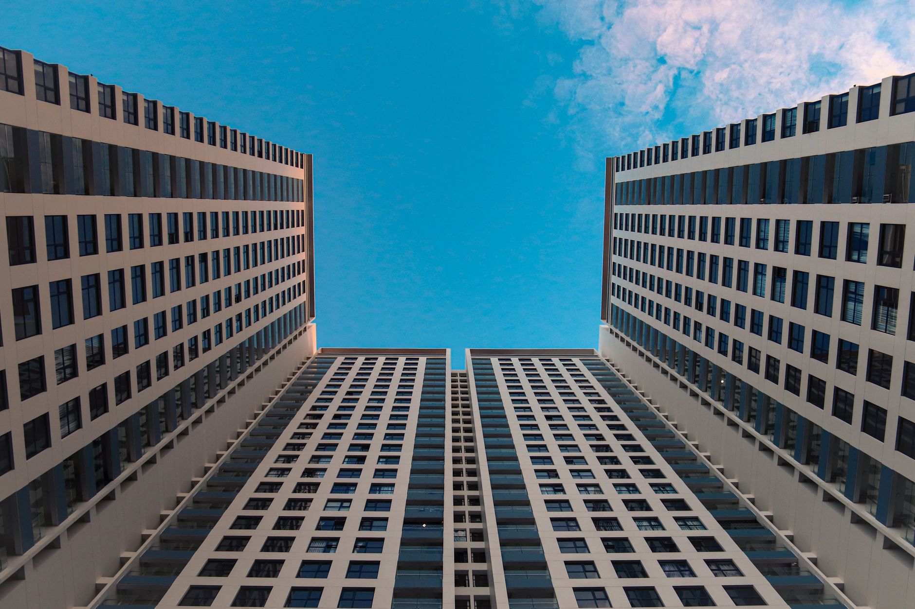 Dynamic low-angle view of modern skyscrapers against a clear blue sky, showcasing symmetrical architectural lines.