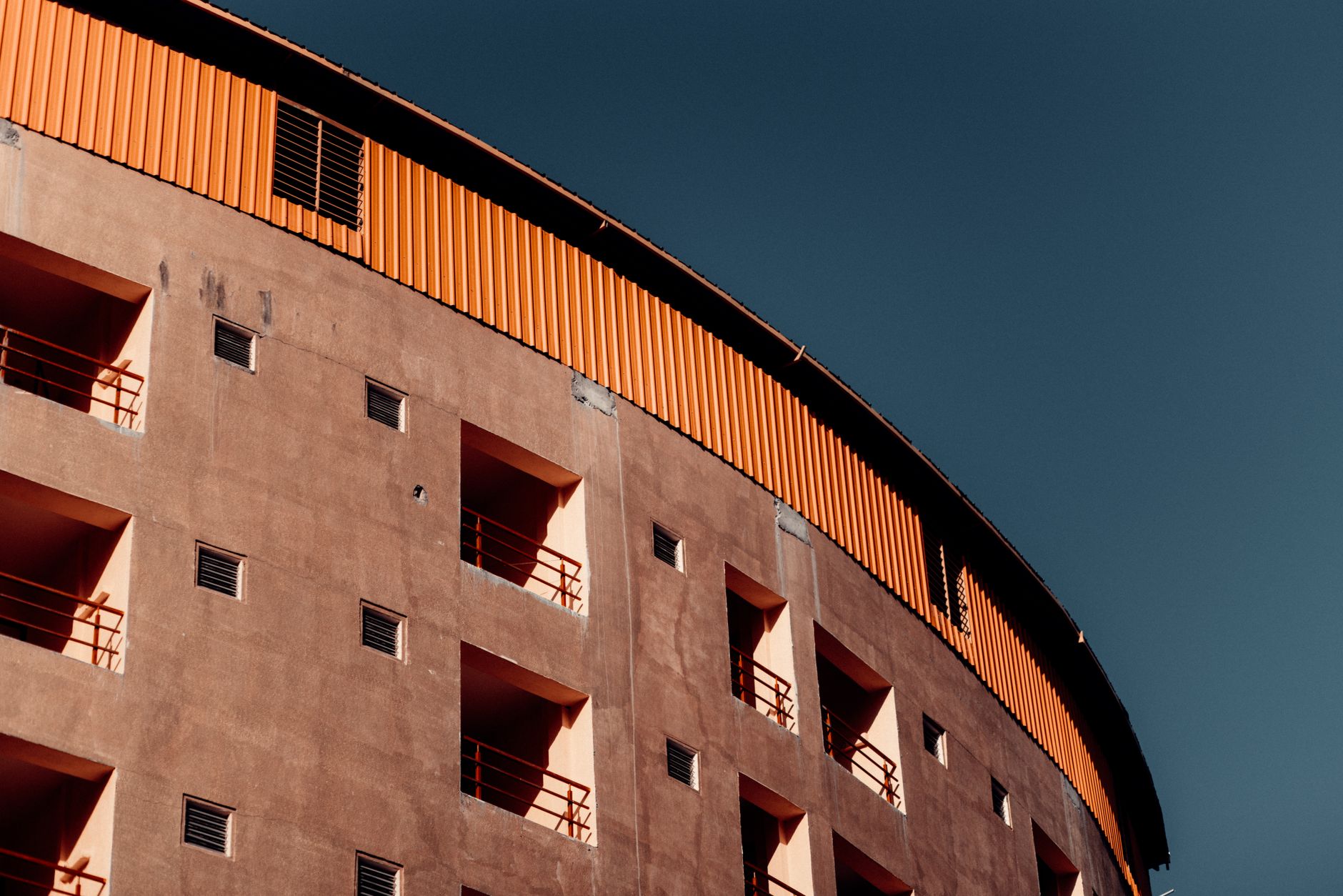 A striking facade of a curved apartment building with balconies under a clear blue sky.