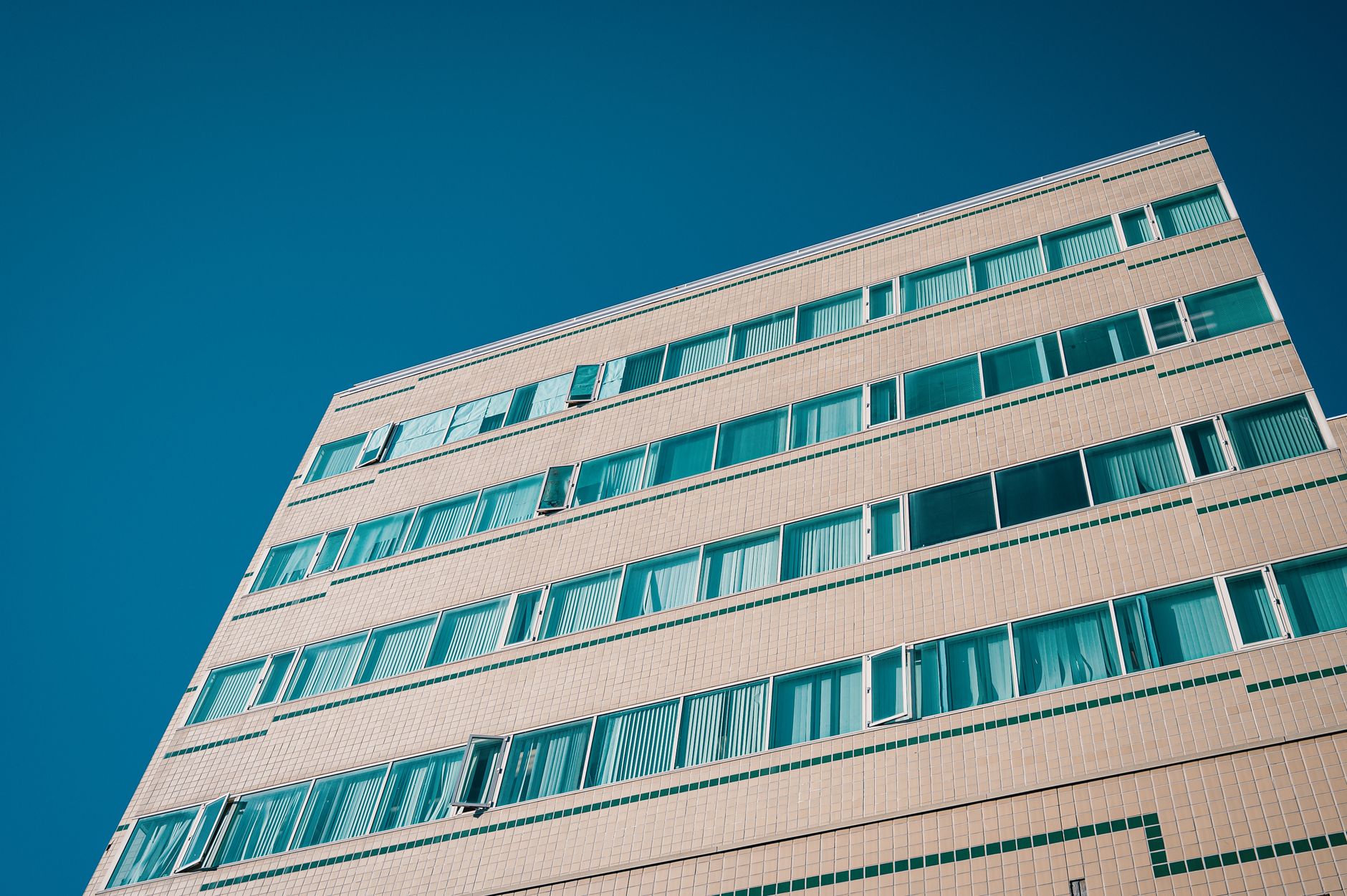 Low angle view of a modern multi-storey building with geometric patterns and blue windows against a clear sky.