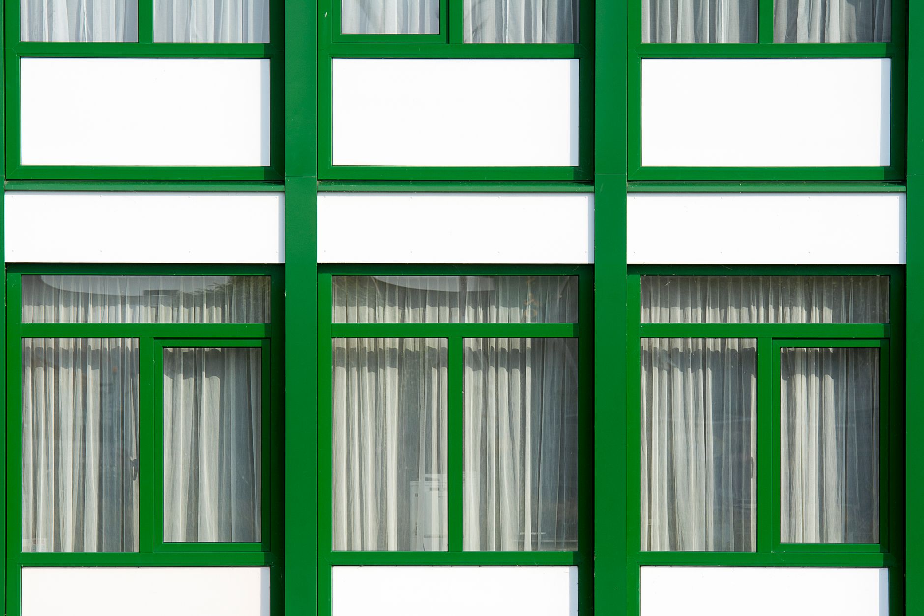Close-up of modern building facade with green frames and curtains.