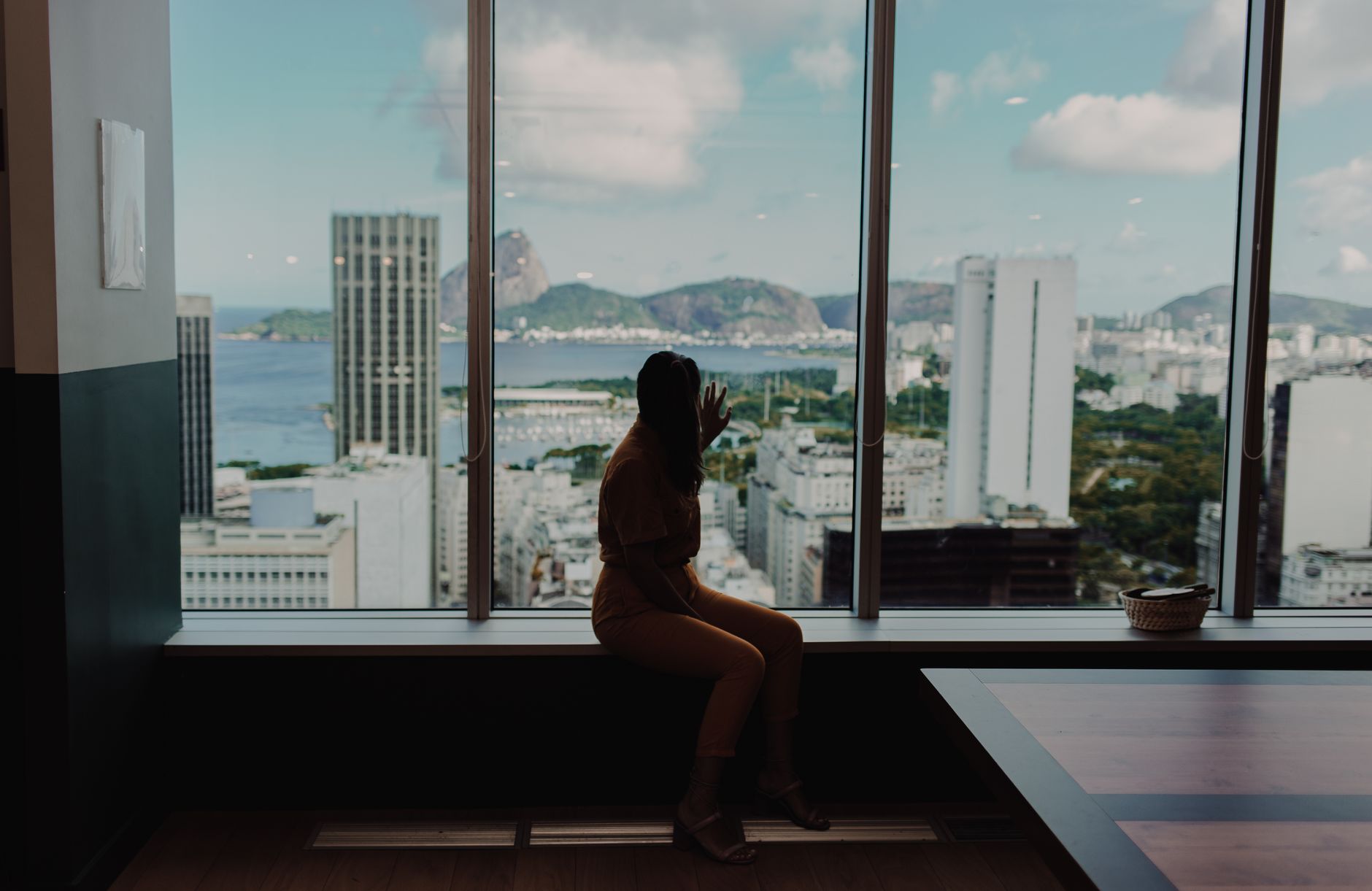 Silhouette of a person sitting by a window with a view of Sugarloaf Mountain in Rio de Janeiro.