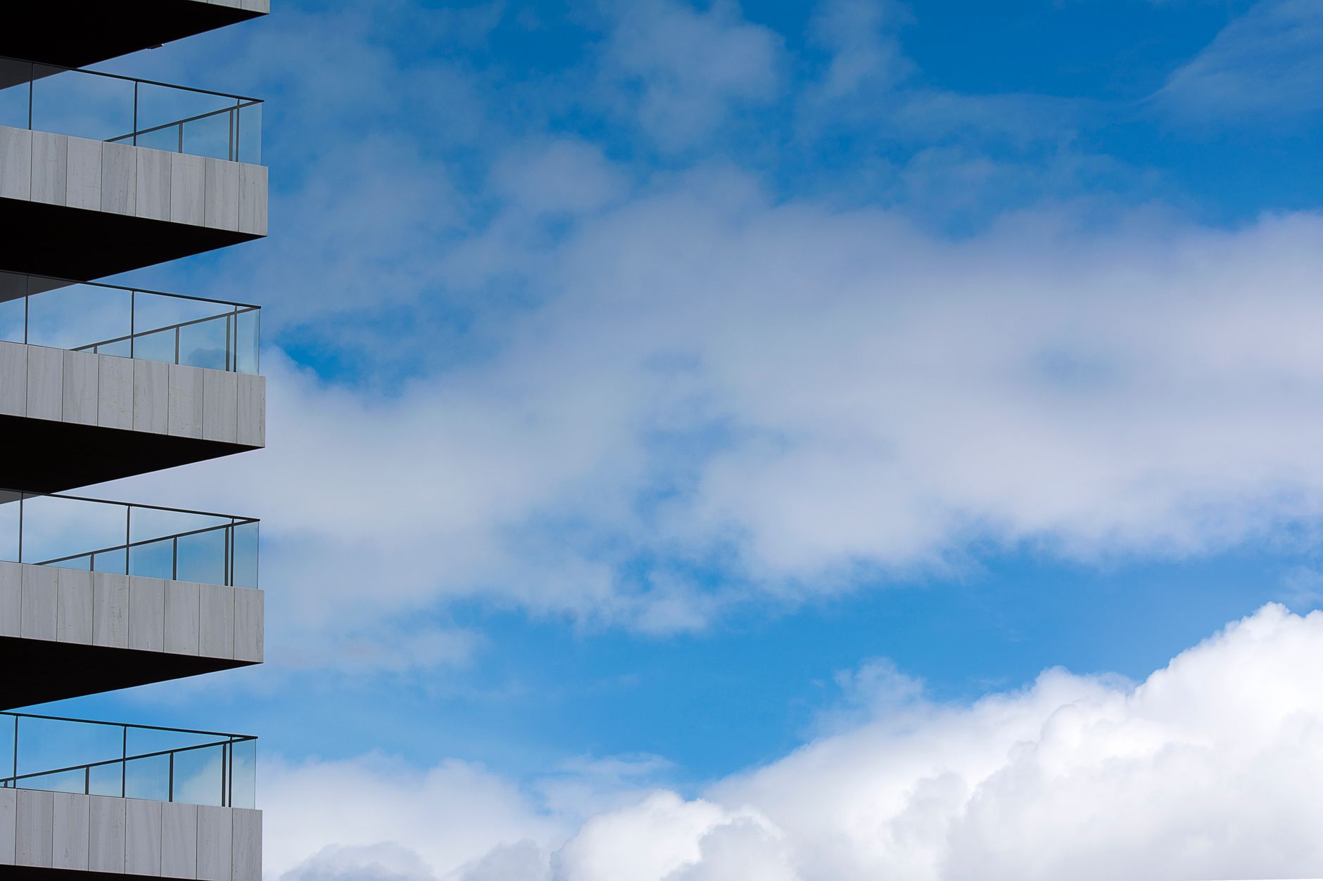 Modern building balconies against a blue sky with fluffy clouds.