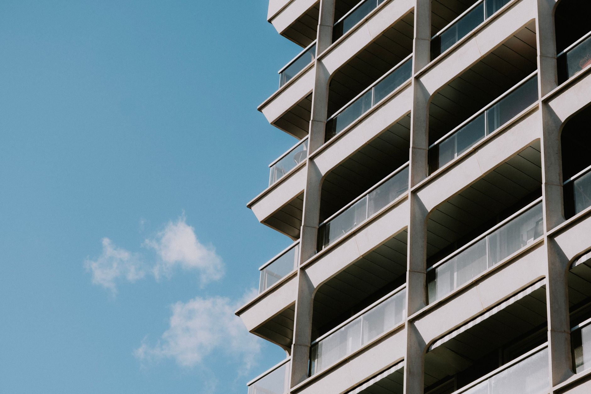 Perspective view of a modern high-rise building featuring balconies against a clear blue sky.