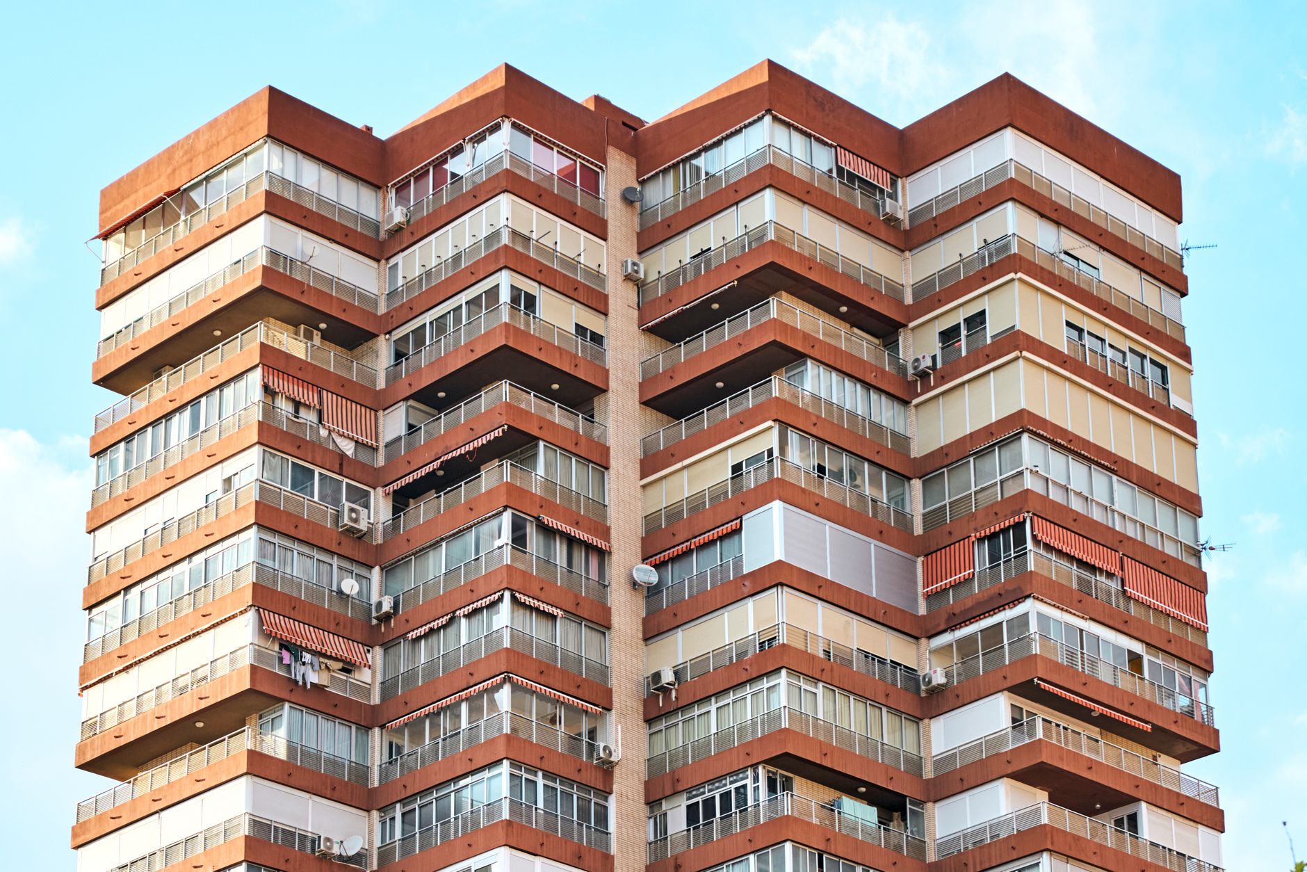 Close-up of a modern multi-story residential building with red and beige facade against a clear blue sky.