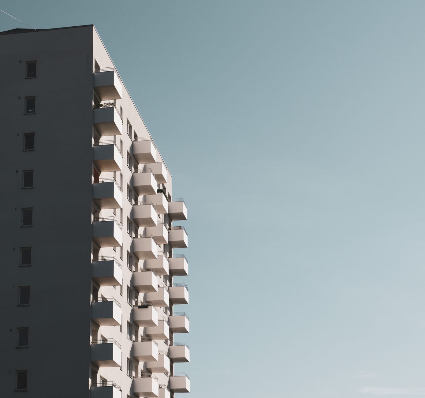 Minimalist view of a concrete apartment building with balconies against a clear sky.
