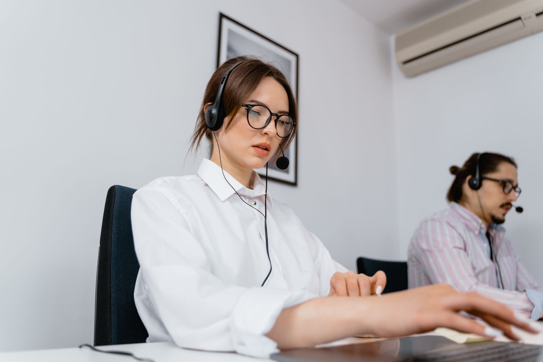 Two customer support agents wearing headsets working at their desks in a modern office setting.