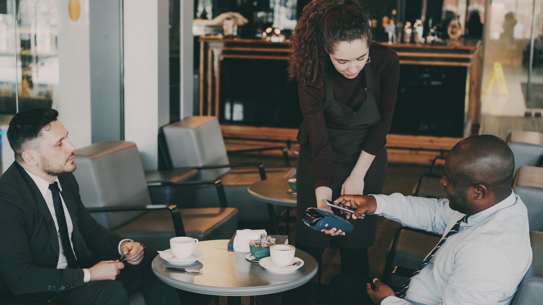 Business professionals enjoy coffee while making payment in a cozy cafe.