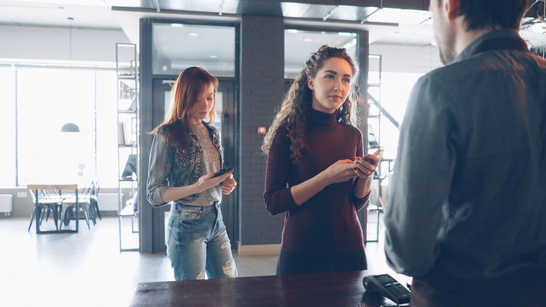 Three young adults engage at a cafe counter, using mobile devices.