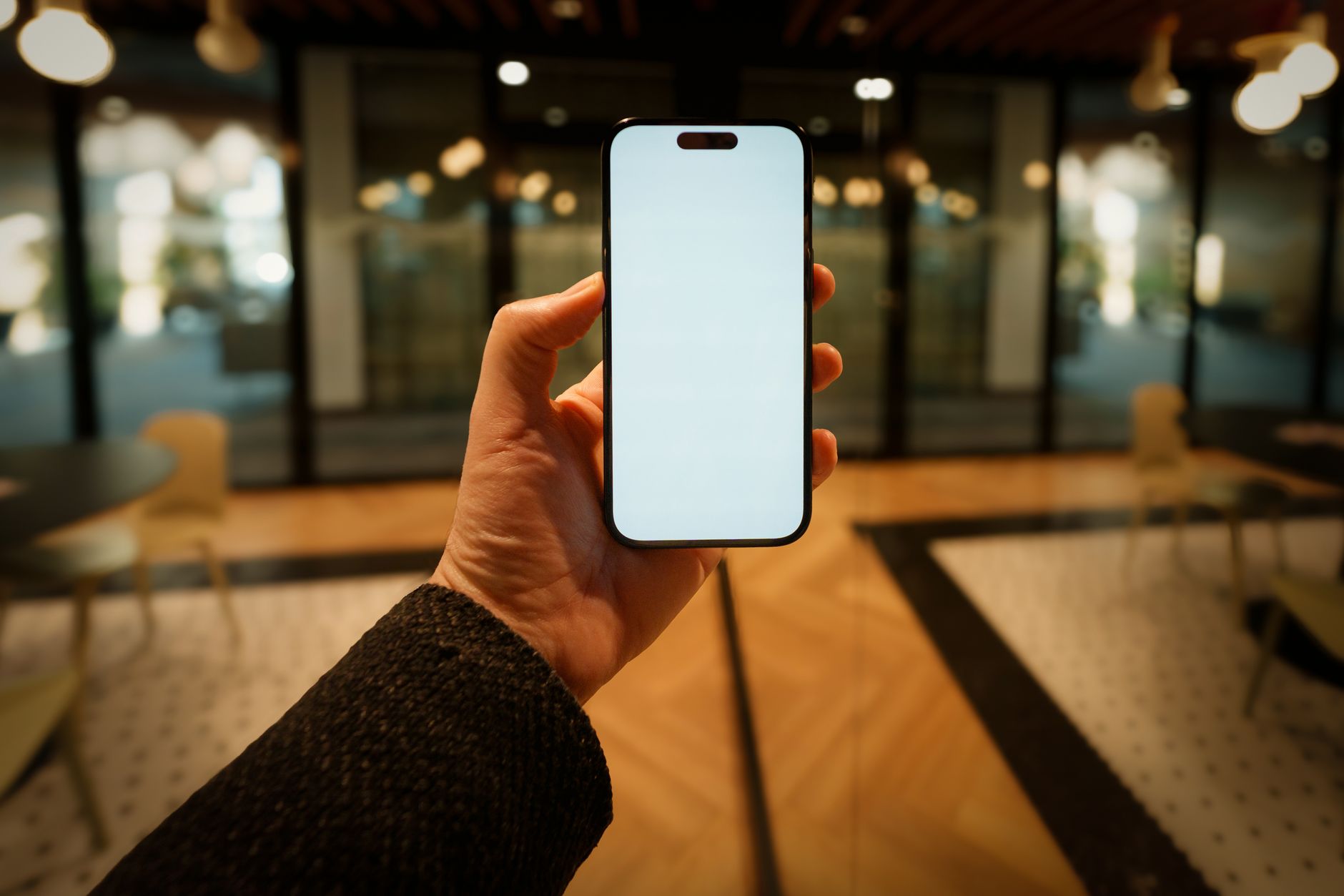 A hand holds a smartphone with a blank screen in a stylish, modern lobby, offering copy space for design use.