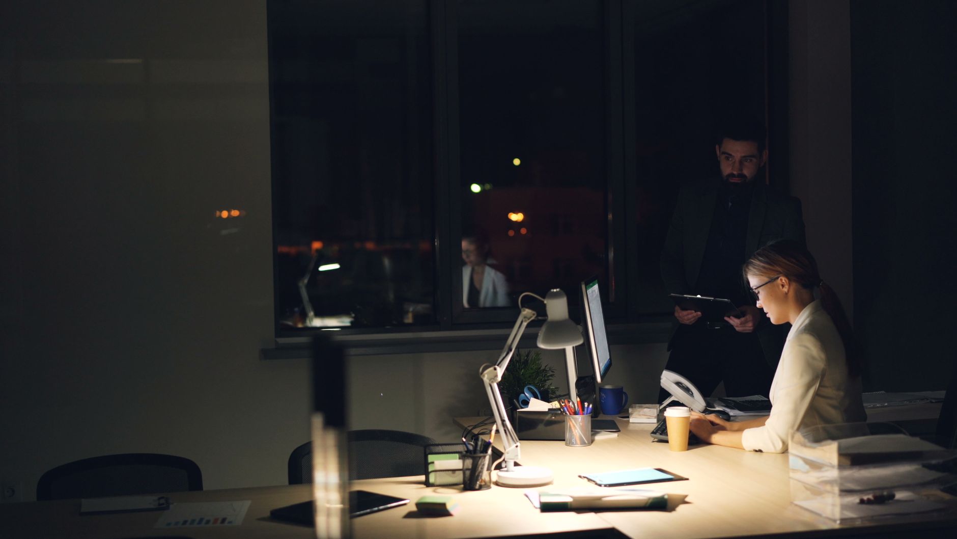Two professionals working late in a dimly lit office, focused on tasks.