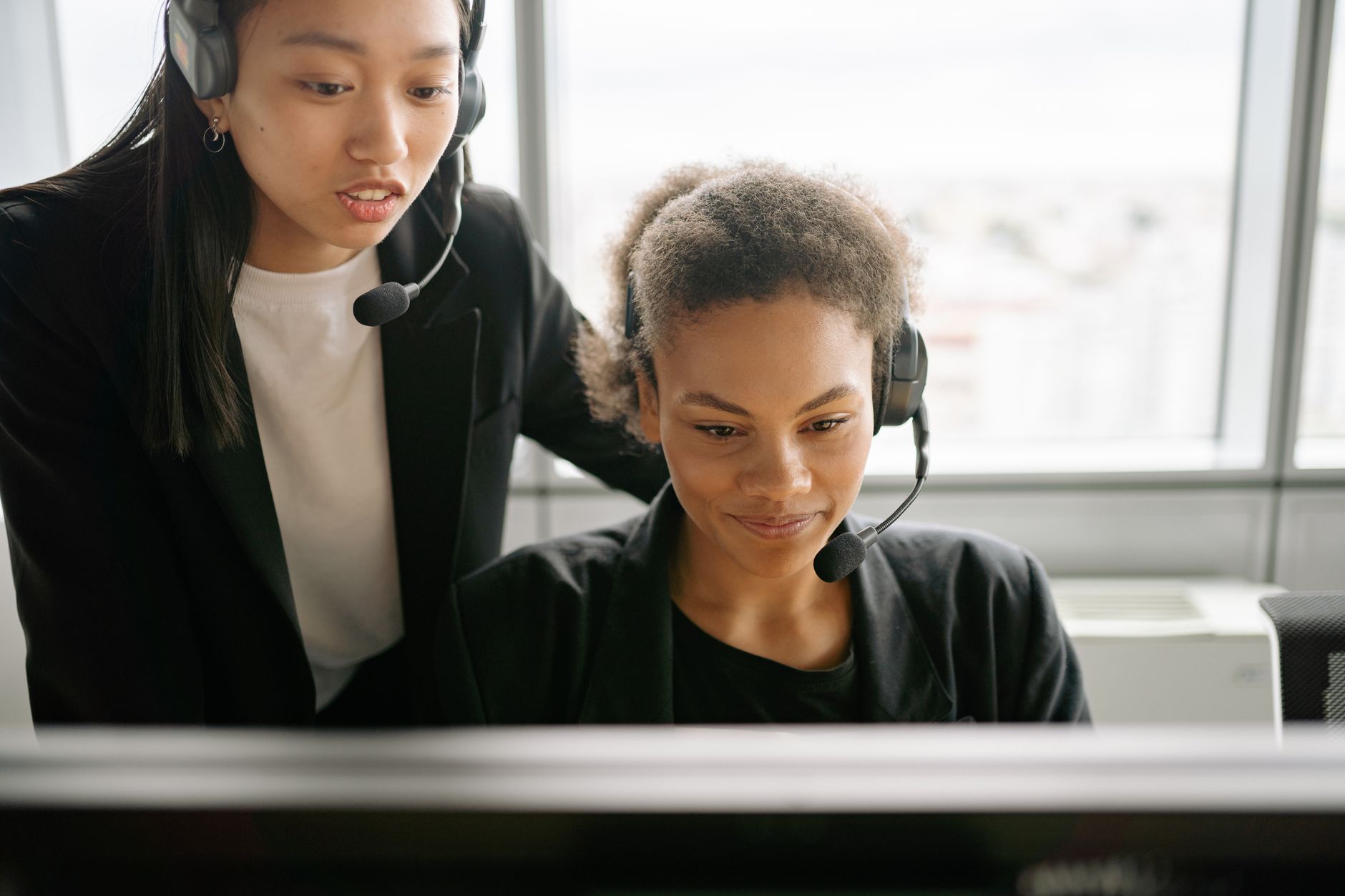 Two women in headsets work together in a modern office, focusing on teamwork and communication.