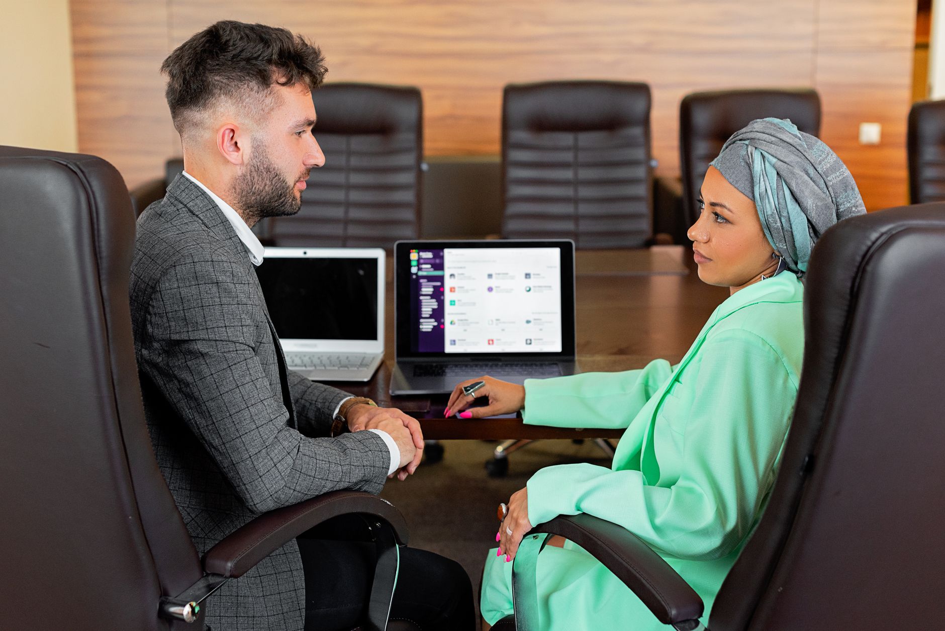 Professional business meeting with two diverse individuals using laptops in a modern conference room.
