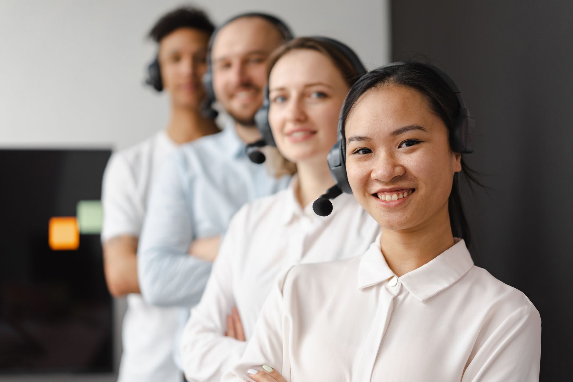 A diverse group of smiling call center agents with headsets, standing together indoors.