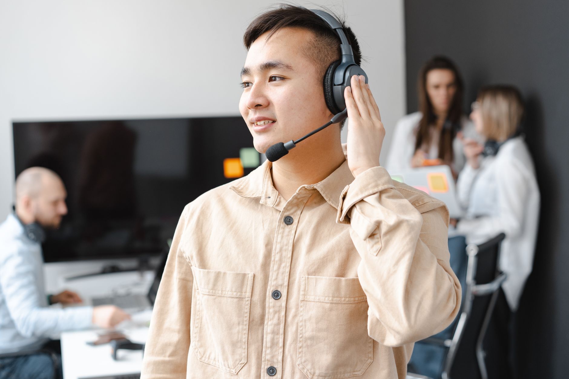 Asian man in beige shirt smiling with headset in modern office setting.
