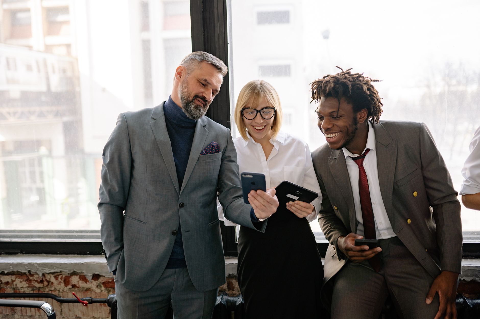 Three colleagues in a modern office sharing a moment over their smartphones.