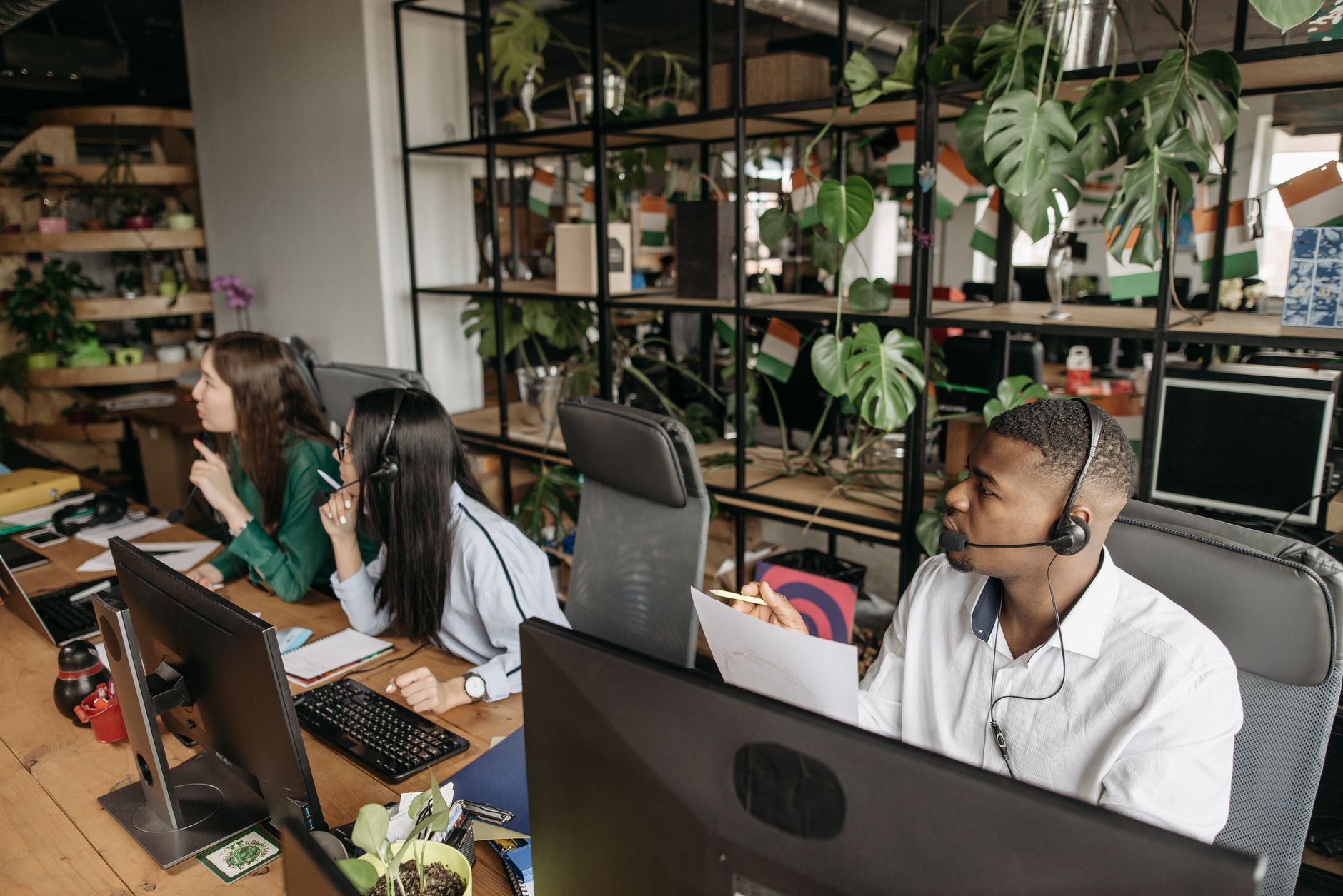 A diverse team collaborates in a modern office with plants and technology.